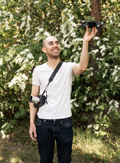 Videograf Viktor som filmar företagsfilmer står med en kamera och drönare i naturlig miljö. 